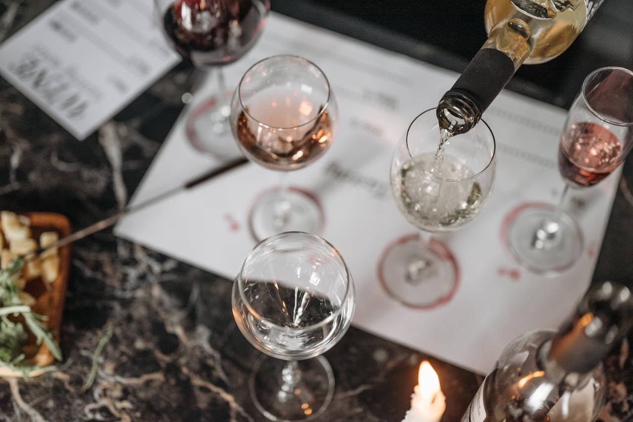 Overhead view of a wine tasting setup on a marble table with white wine being poured and cheese platter nearby.