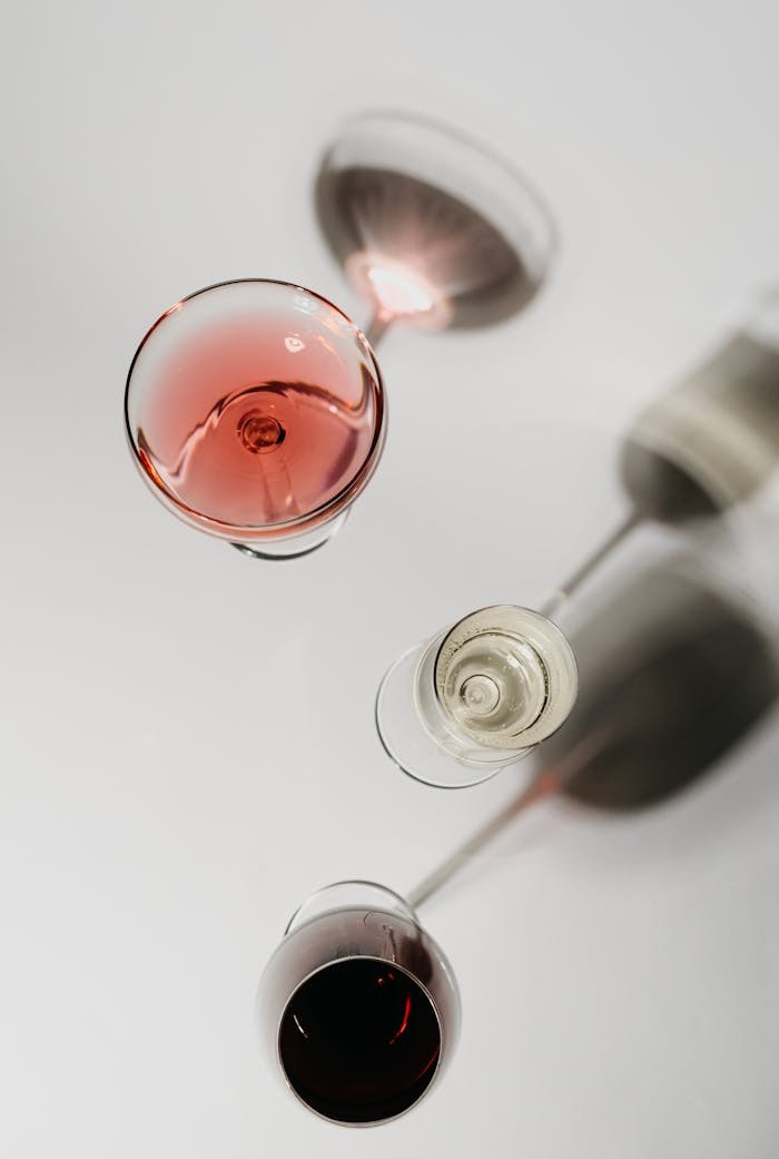 Artistic top view of wine glasses with red, white, and rosé wines on a white surface.